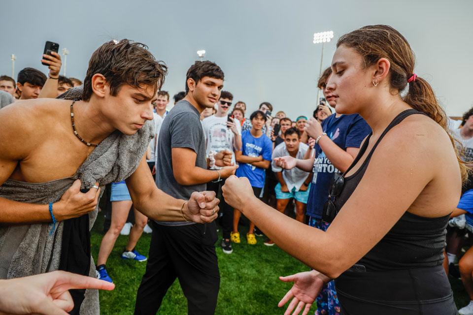 Two students play rock, paper, scissors in front of a crowd